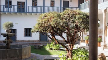 Ein Innenhof mit einem großen Baum, einer Fontäne und einem Gebäude mit Ziegeldach.
