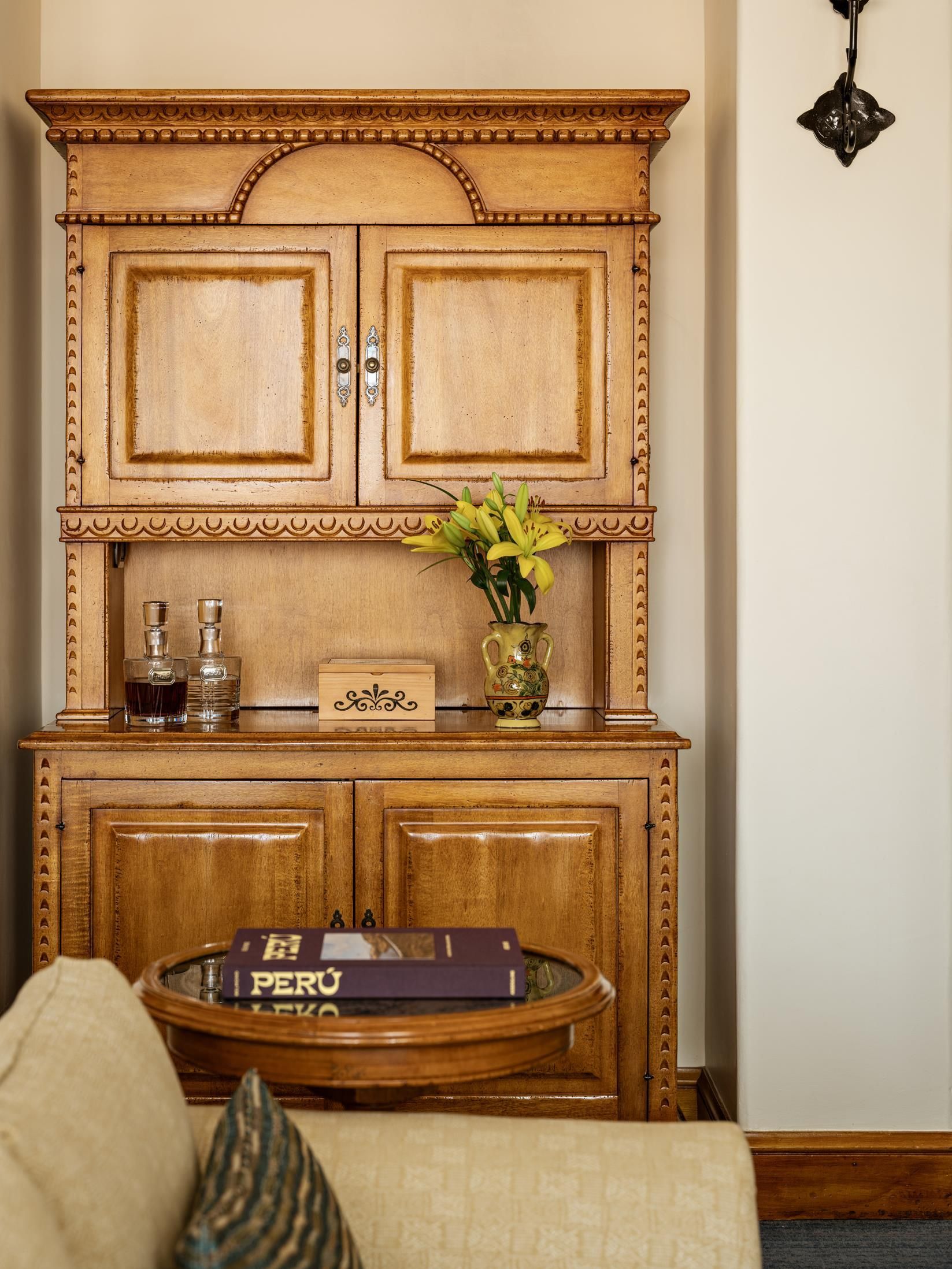 Un meuble en bois à deux portes, un vase avec des fleurs et un livre intitulé « PÉROU » sur une table.
