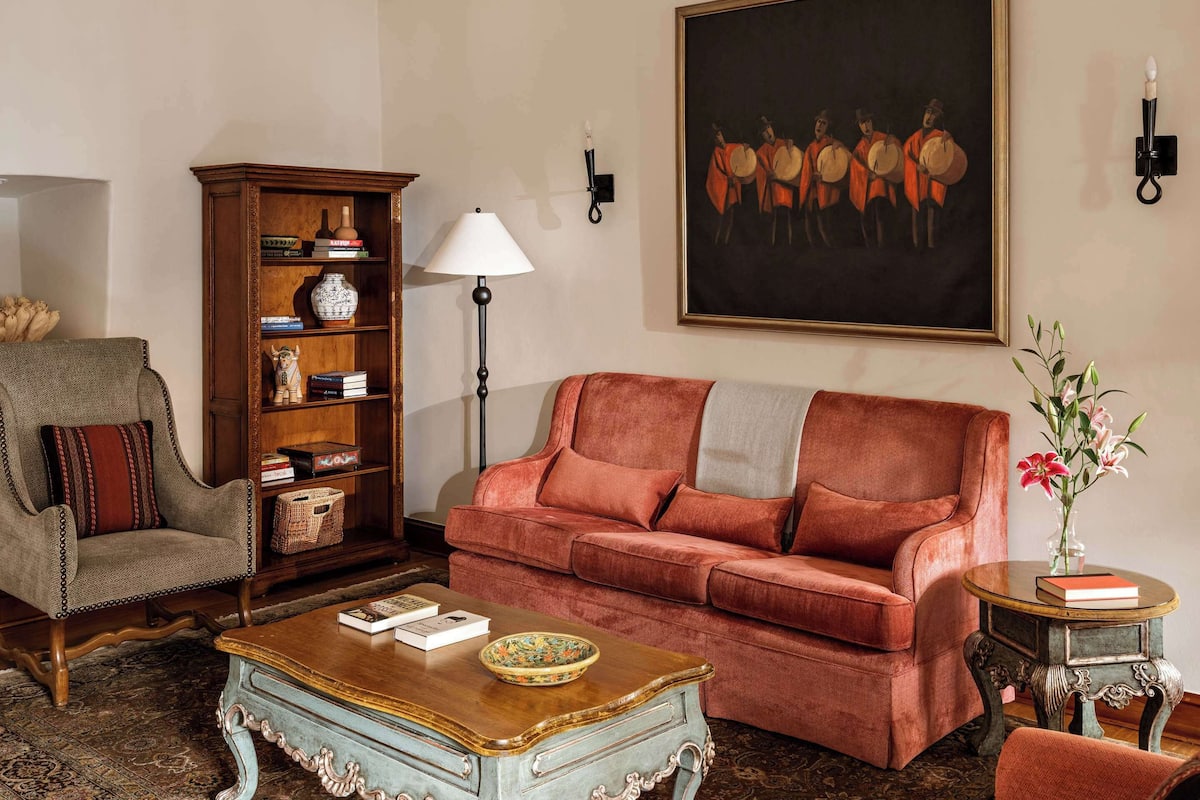 A living room with a chandelier, a sofa, a chair, a side table, a bookshelf, and a painting on the wall.