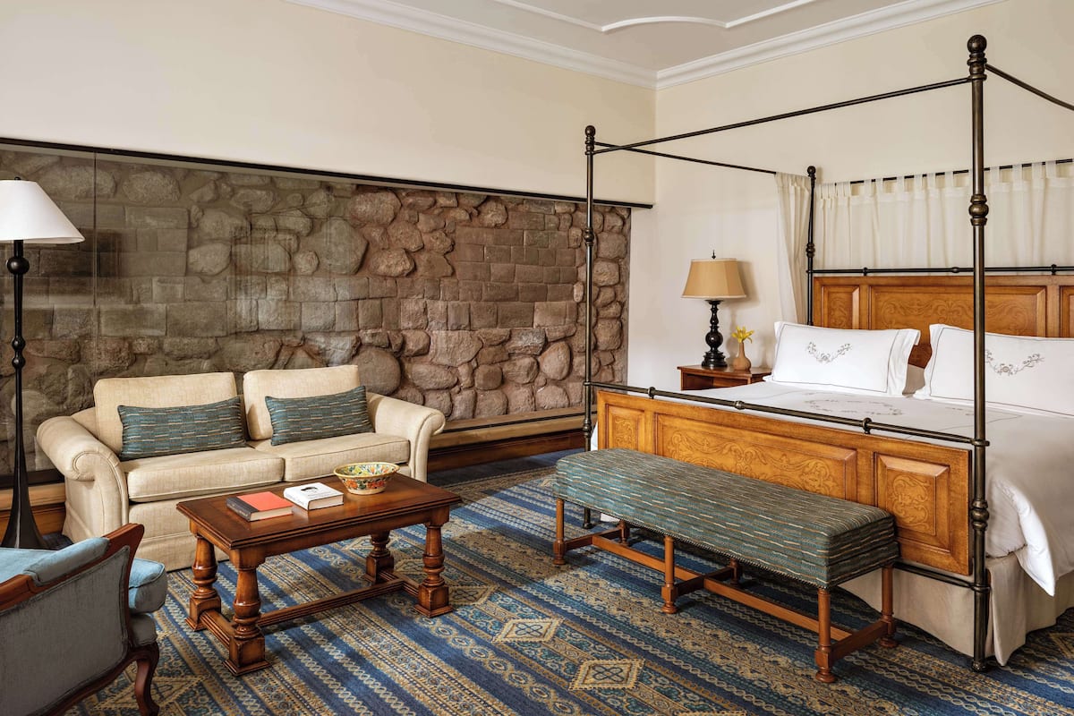 A hotel room with a stone wall, a four-poster bed, a sofa, a bench, and a coffee table.