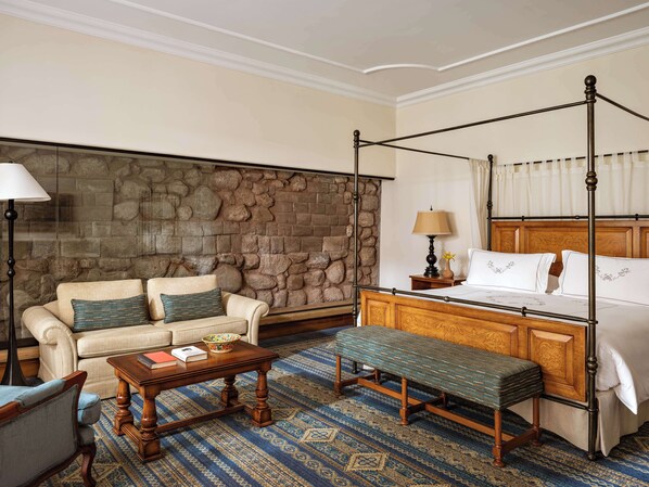 Habitación de hotel con pared de piedra, cama con dosel, sofá, banca y mesa de centro.