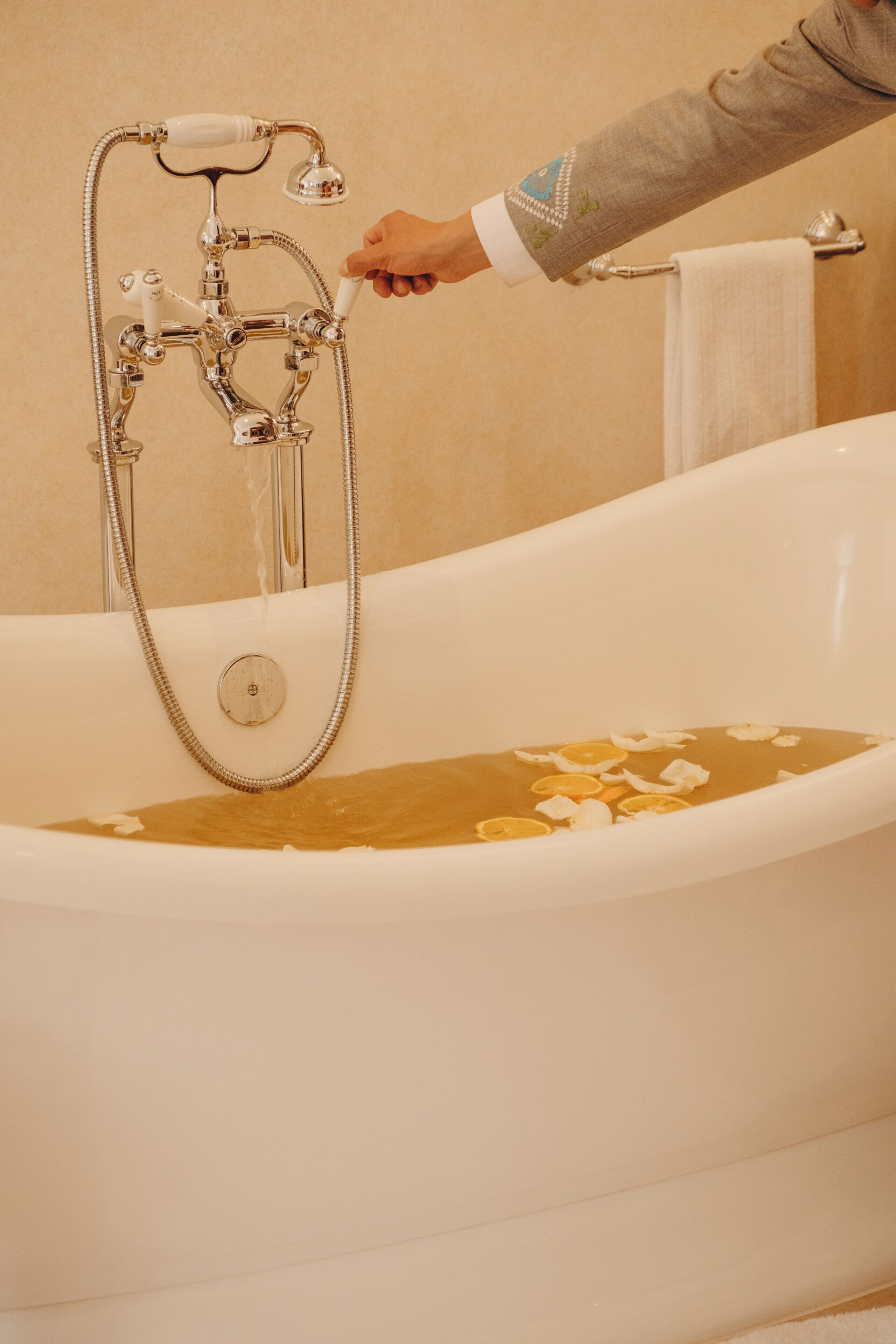 Eine Badewanne mit Duschkopf, eine Hand, die den Wasserfluss reguliert, und ein Handtuch an einem Halter.