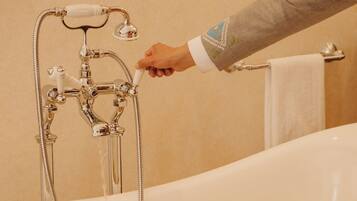 Una bañera con ducha, una mano ajustando el flujo del agua y una toalla colgada en un perchero.