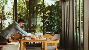 Un restaurante con mesas y sillas de madera, ventanas amplias y lámparas de tela en el techo.