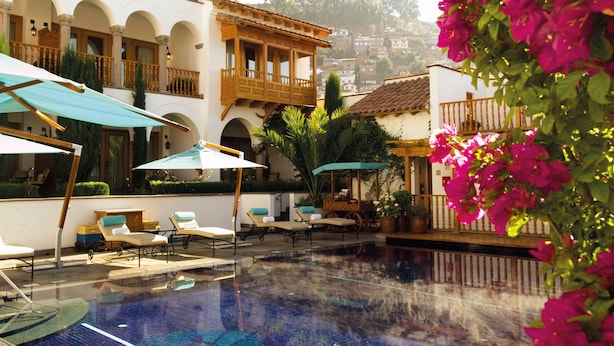 Zona de piscina con sillas de descanso y sombrillas, rodeada de edificios con balcones y ventanas de arco.