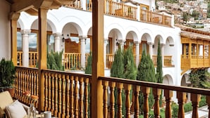 Un espacio al aire libre cubierto con barandilla de madera, una mesa con sillas y vistas a un edificio blanco con balcones.
