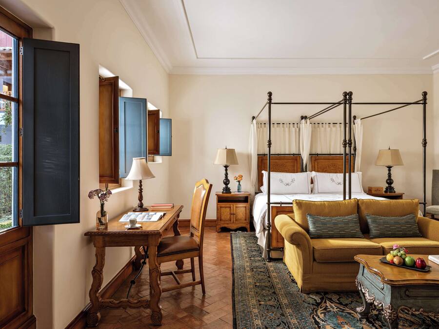 A room with a four-poster bed, a sofa, a table with a lamp, and a chair.
