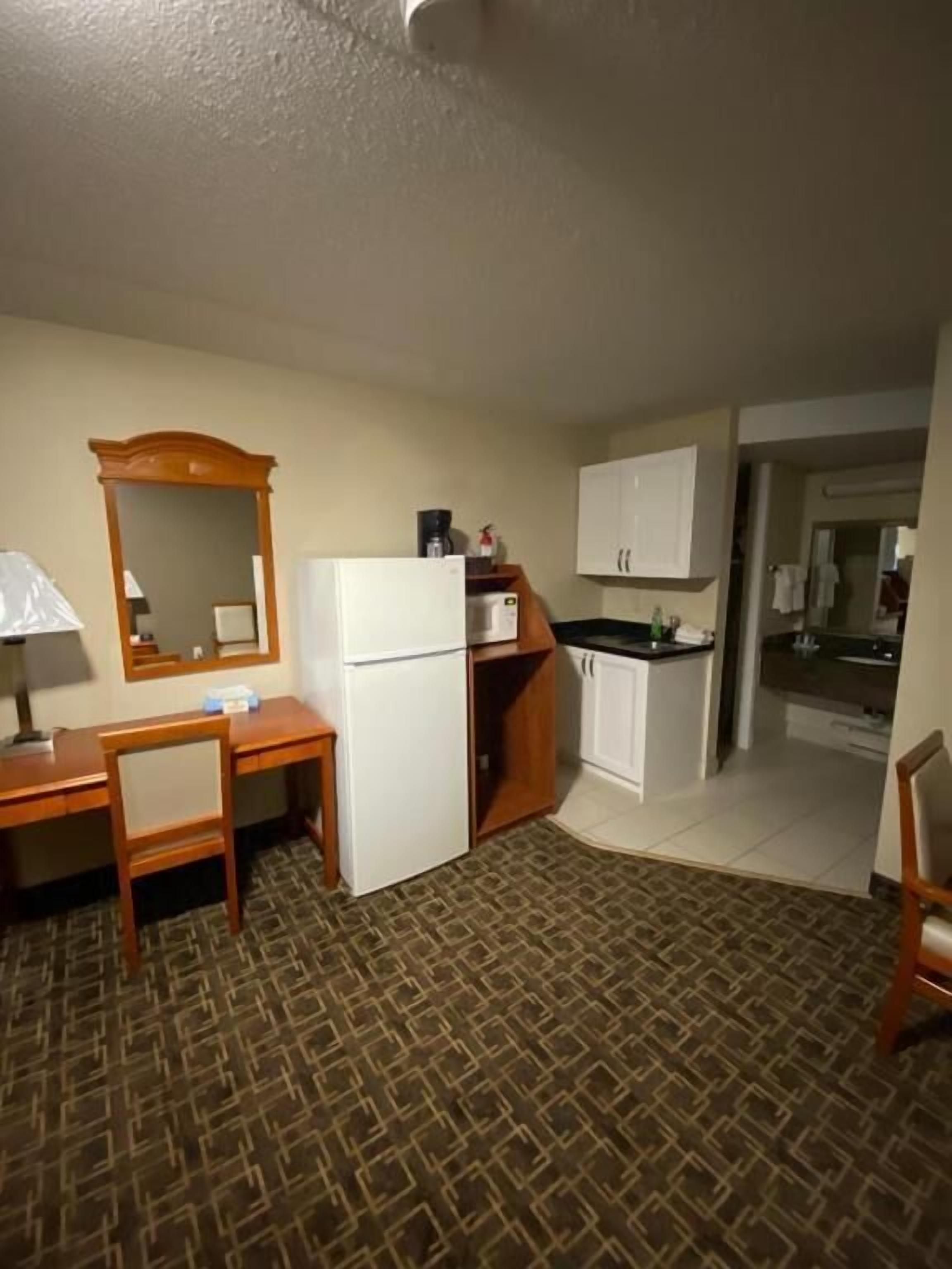 Habitación de hotel pequeña con kitchenette, un escritorio, una silla y alfombra estampada.