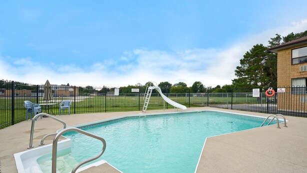 A swimming pool with a slide, a ladder, and a lifebuoy, surrounded by a fence and a building. - Angus Inn (Essa)