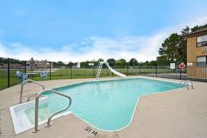 A swimming pool with a slide, a ladder, and a lifebuoy, surrounded by a fence and a building.