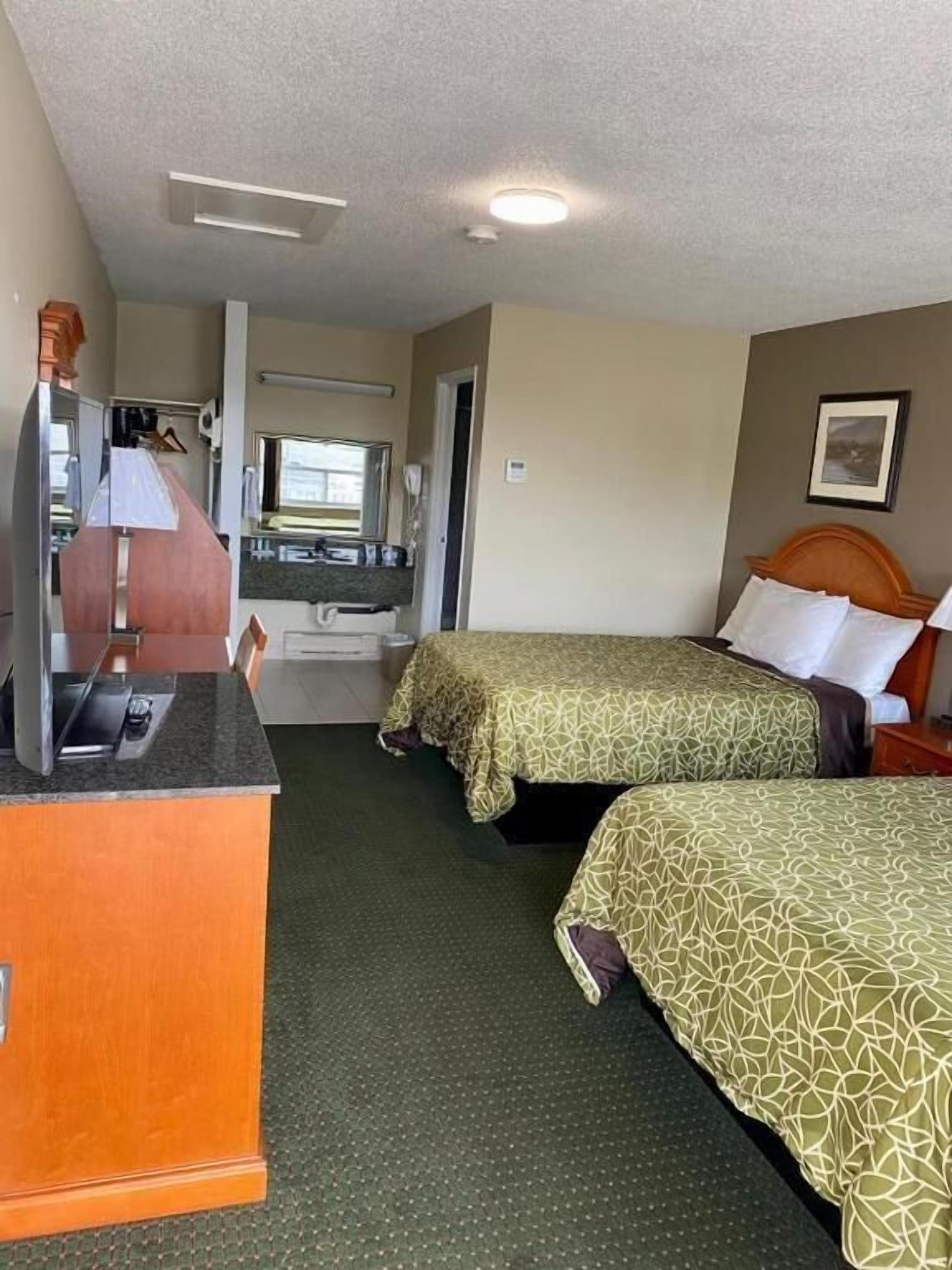 Une chambre d’hôtel avec deux lits, un bureau avec une télévision et une salle de bain visible par une porte ouverte.