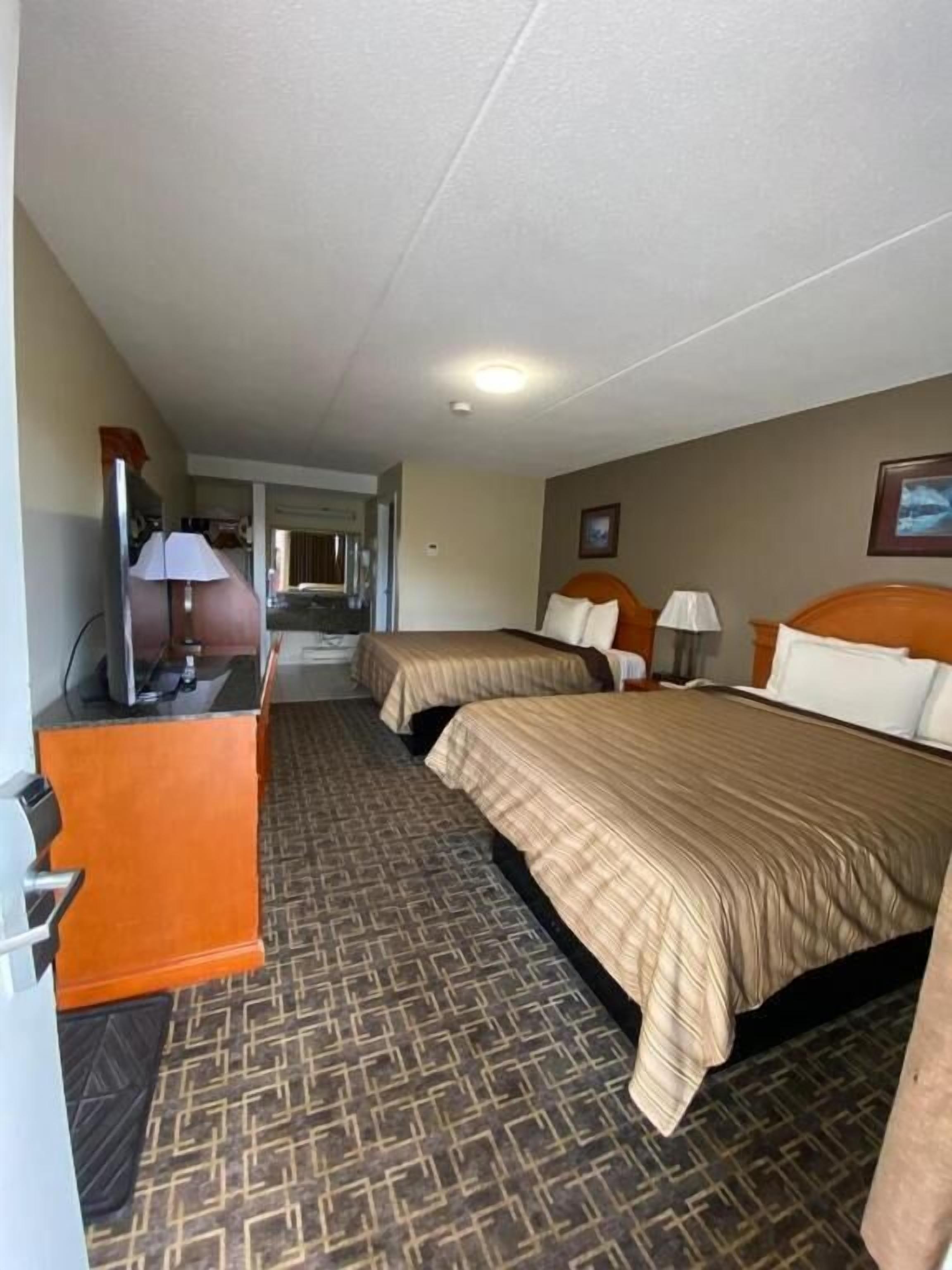 Habitación de hotel con dos camas, un escritorio y vista al pasillo.