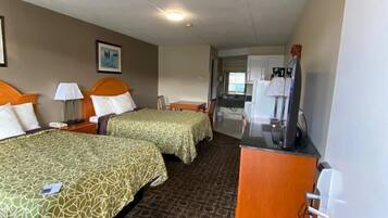 Quarto de hotel com duas camas, uma escrivaninha, uma cadeira e uma cozinha compacta.