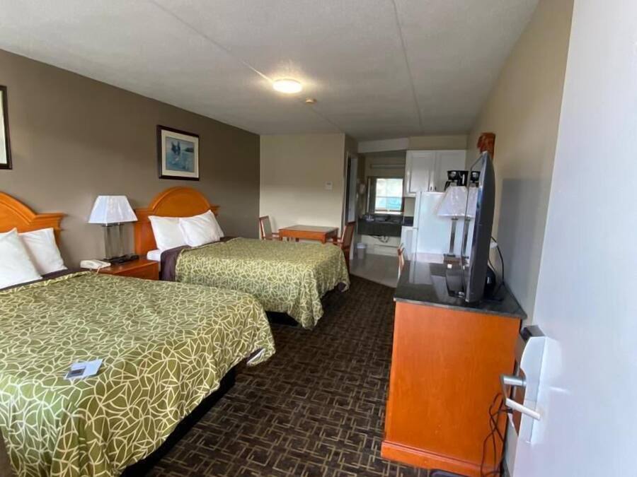 Quarto de hotel com duas camas, uma escrivaninha, uma cadeira e uma cozinha compacta.