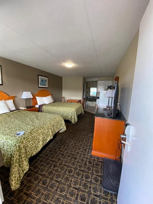 A hotel room with two beds, a desk, a chair, and a kitchenette.