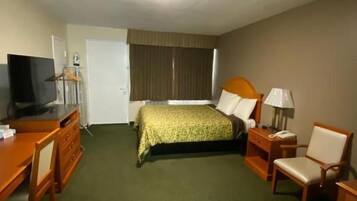 A hotel room with a bed, a desk, a chair, a TV, and a lamp.