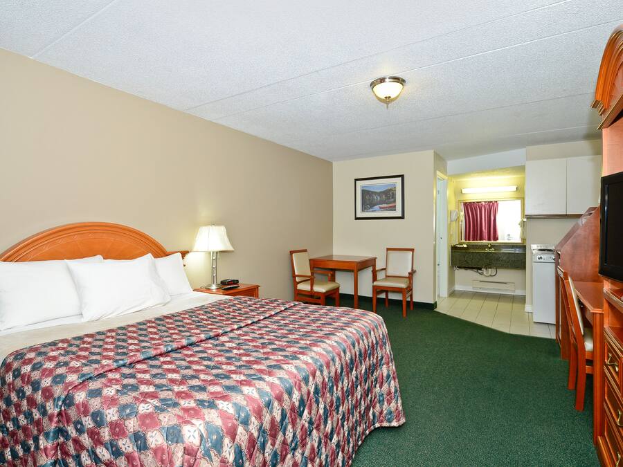 A hotel room with a bed, a desk, a television, and a kitchenette.