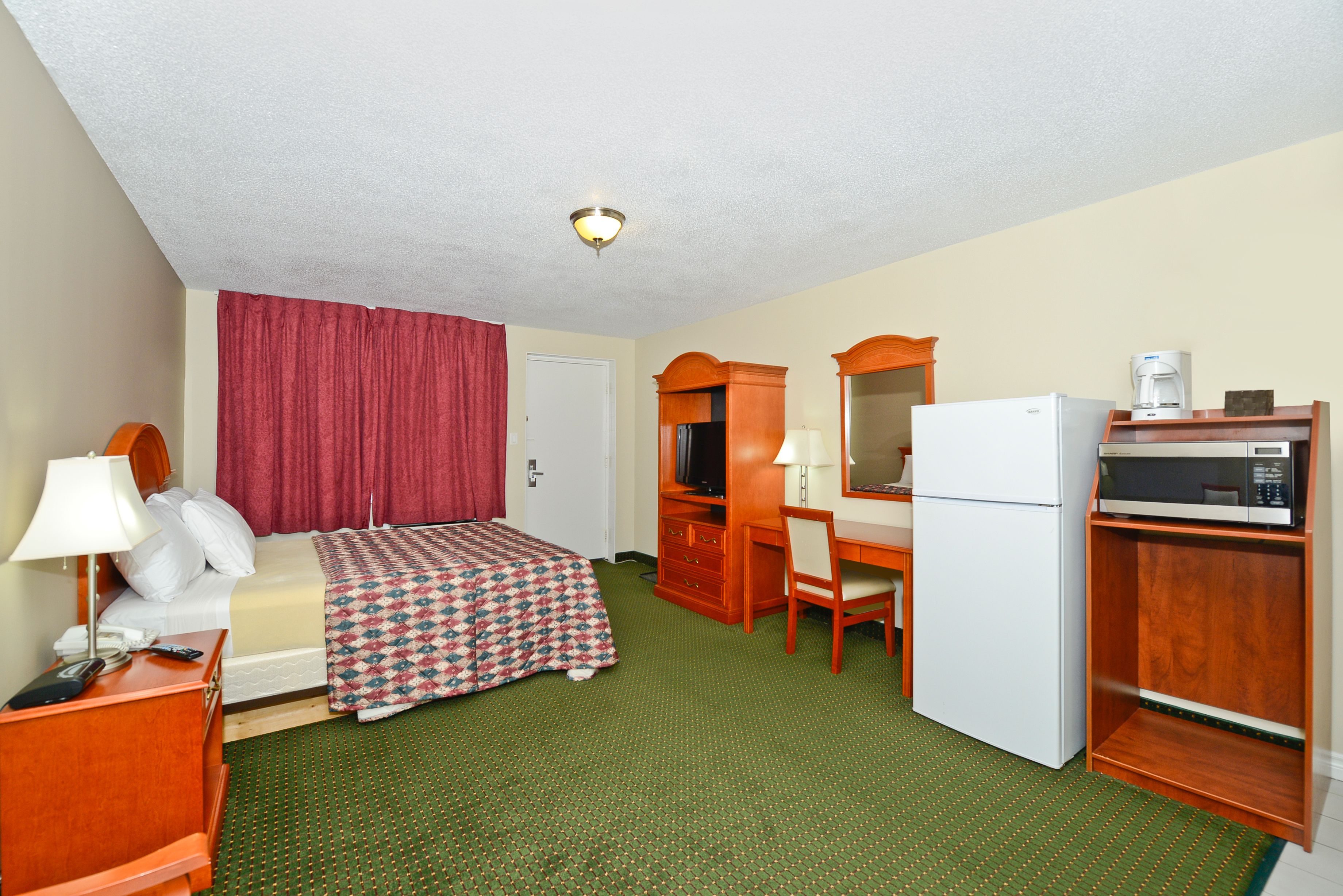 Habitación de hotel con cama, escritorio, silla, refrigerador, microondas y televisor.