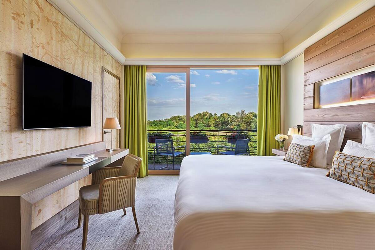Une chambre d’hôtel équipée d’un lit, d’un bureau, d’une chaise, d’une télévision et d’un balcon donnant sur un paysage verdoyant.