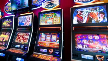 A row of slot machines with various game themes and a neon sign above them.
