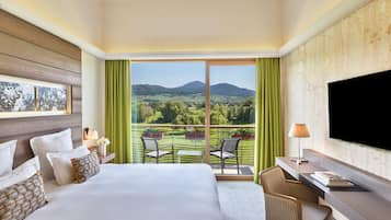 Habitación de hotel con una cama grande, un escritorio, un televisor y un balcón con vistas al campo.