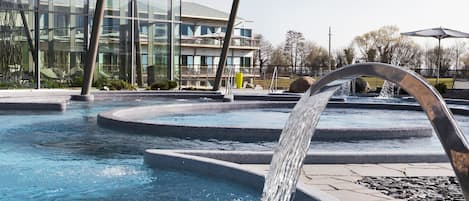 A swimming pool with a water feature, surrounded by a covered area with glass walls.