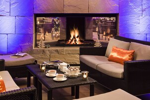 Un rincón al aire libre acogedor con chimenea de piedra, muebles de mimbre y una mesa dispuesta con té y aperitivos.