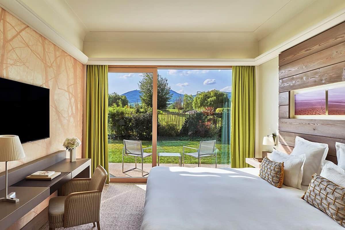 Une chambre d’hôtel équipée d’un lit, d’un bureau, d’une télévision et offrant une vue sur un jardin et des montagnes.