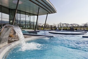 Relax by the pool surrounded by lush trees and a glass building with a curved roof.