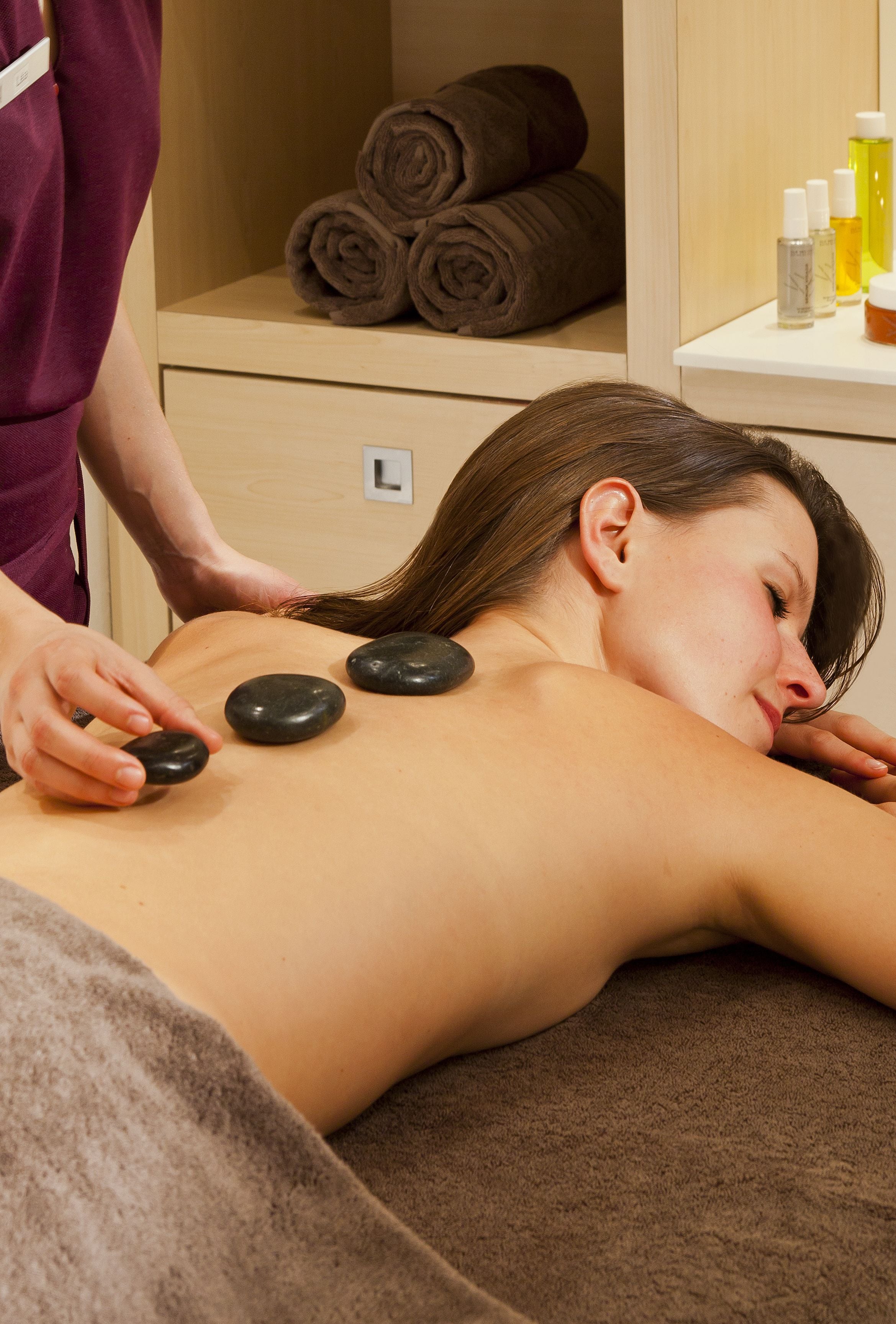 A massage therapy session with a person lying face down receiving stone massage on their back.