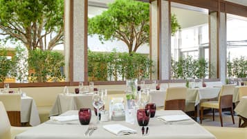 Un restaurante con mesas dispuestas para comer, amplias ventanas con vistas a árboles y un interior moderno y cuidado.