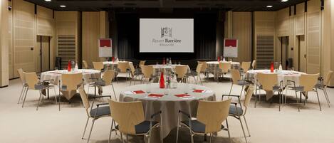 A conference room with round tables and chairs, a large screen displaying 'Resort Barrière', and a stage with curtains.