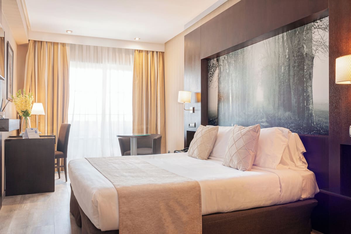 Une chambre d’hôtel avec un grand lit, un bureau avec une chaise, une petite table et un grand tableau abstrait accroché au mur.