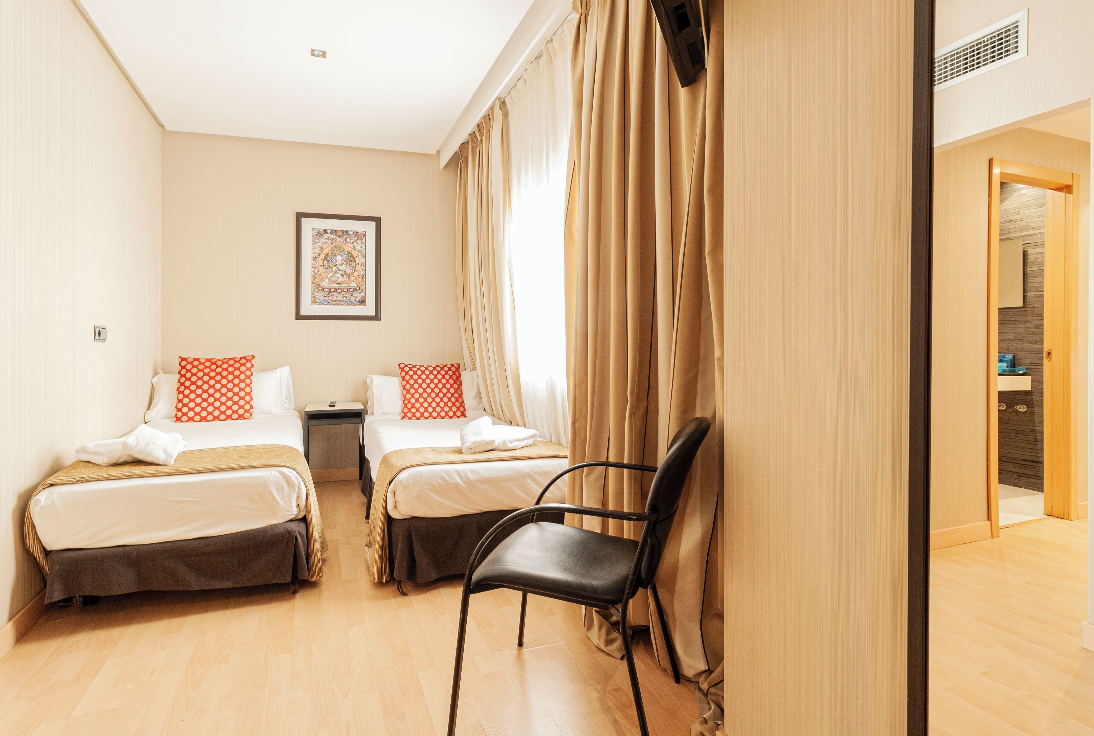 A hotel room with two beds, a chair, and a bathroom visible through an open door.