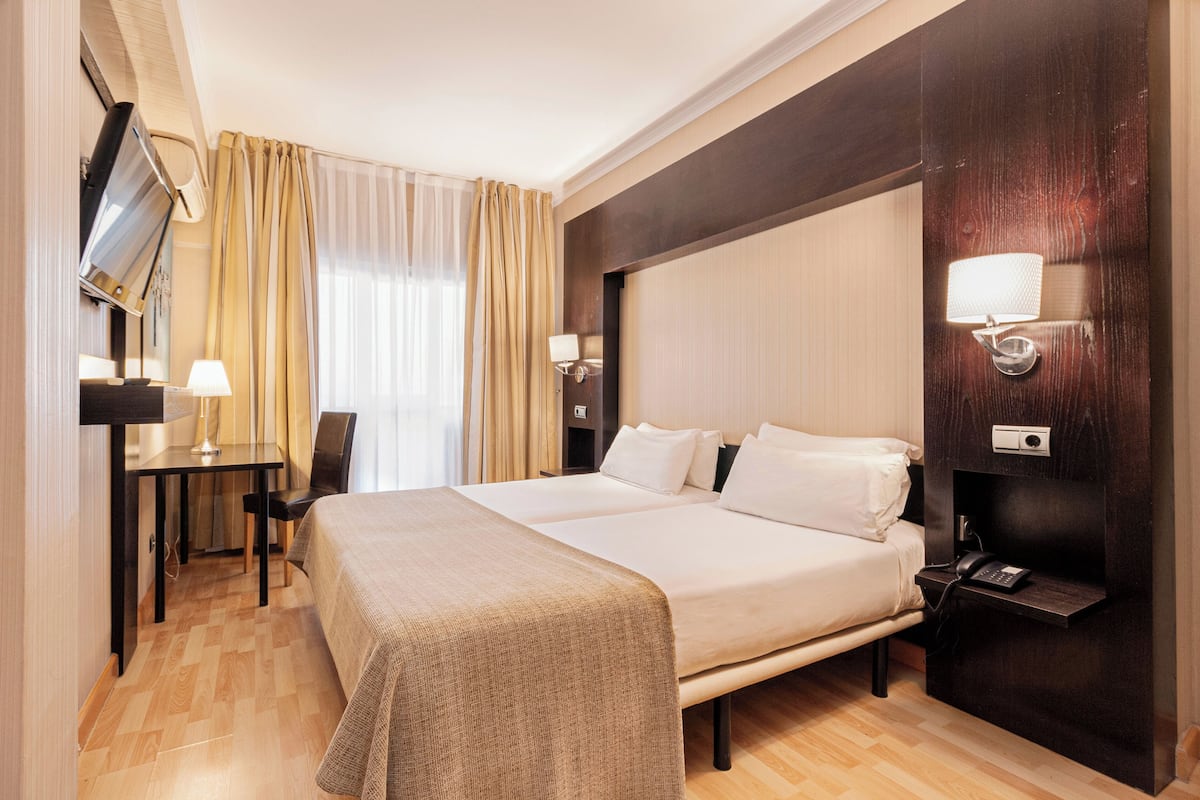 Une chambre d’hôtel avec un grand lit, un bureau avec une chaise, une télévision et une table de chevet avec une lampe.
