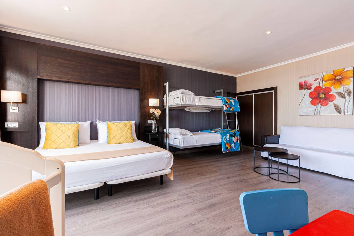 Une chambre d’hôtel avec un grand lit, un lit superposé, un canapé, une petite table et une chaise.