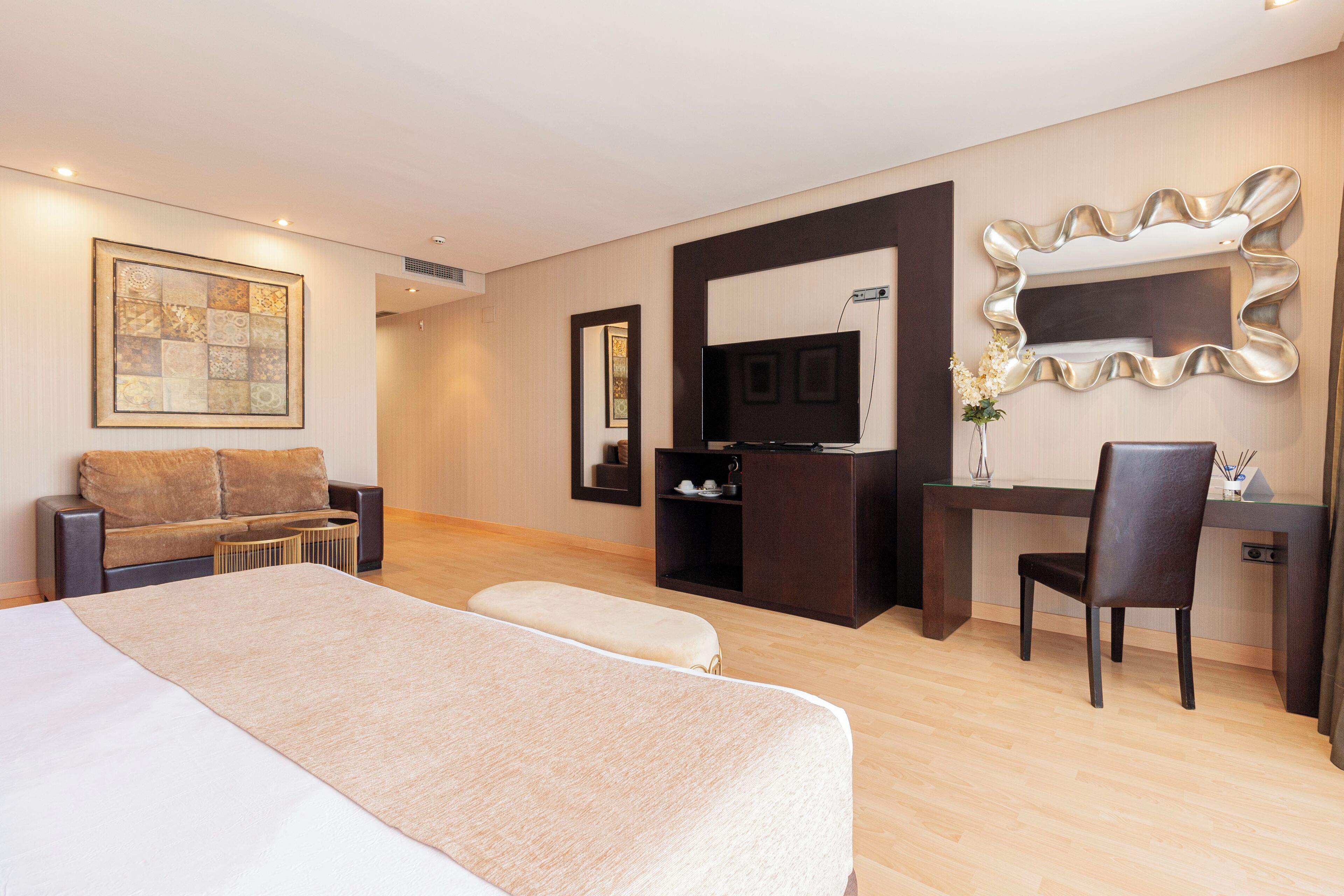 A hotel room with a large bed, a desk, a chair, a television, and a decorative mirror.