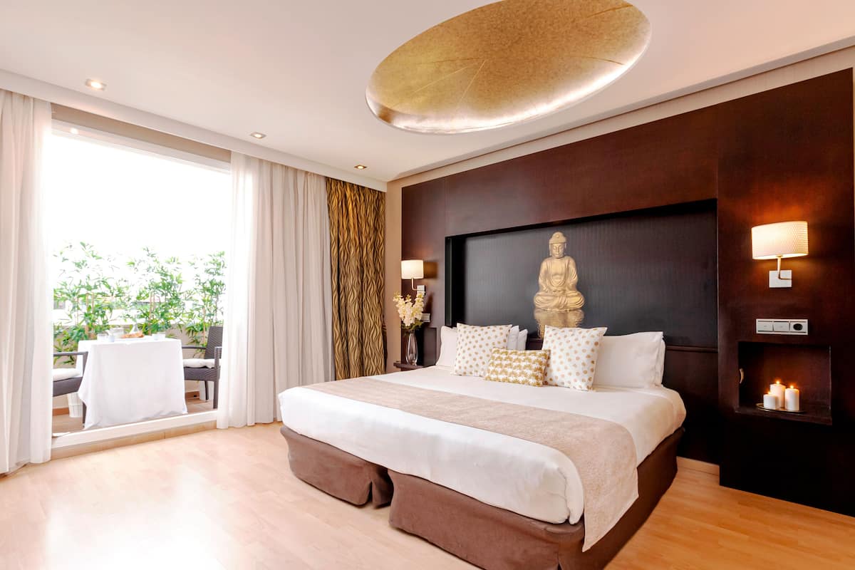 Une chambre d’hôtel moderne avec un grand lit, une statue au mur et une vue sur la verdure.