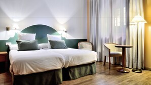 A hotel room with a double bed, two bedside lamps, a chair, a small round table, and a large window with curtains. - Hotel AHC Palacio Coria (Coria)
