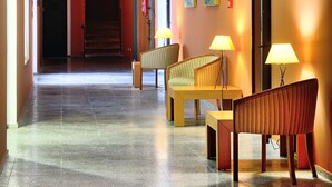 A hotel lobby with a long corridor, seating area with lamps, and artwork on the walls. - Hotel AHC Palacio Coria (Coria)