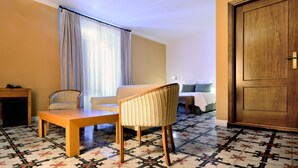 A hotel room with a wooden door, a sofa, two striped chairs, a small table, and a patterned floor. - Hotel AHC Palacio Coria (Coria)