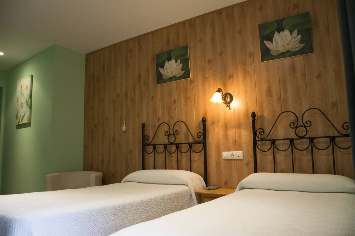 Una habitación de hotel con dos camas individuales, paneles de madera en las paredes y una lámpara fijada a la pared.
