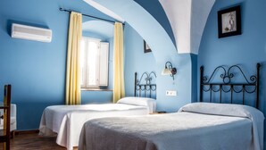 Une chambre avec deux lits, une fenêtre avec des rideaux jaunes, un climatiseur et une lampe fixée au mur.
