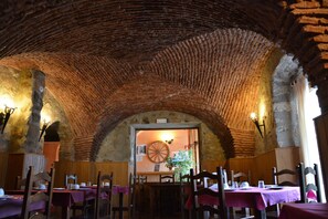 A rustic dining area with brick arches, wooden tables, and chairs.