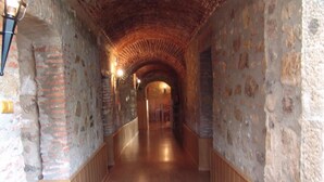 Un couloir aux murs de pierre, avec des bancs en bois et un plafond en briques.