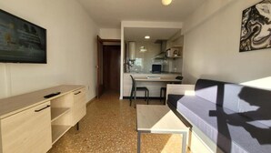 Un espace de vie compact comprenant un coin cuisine, un canapé, une petite table et un téléviseur fixé au mur.