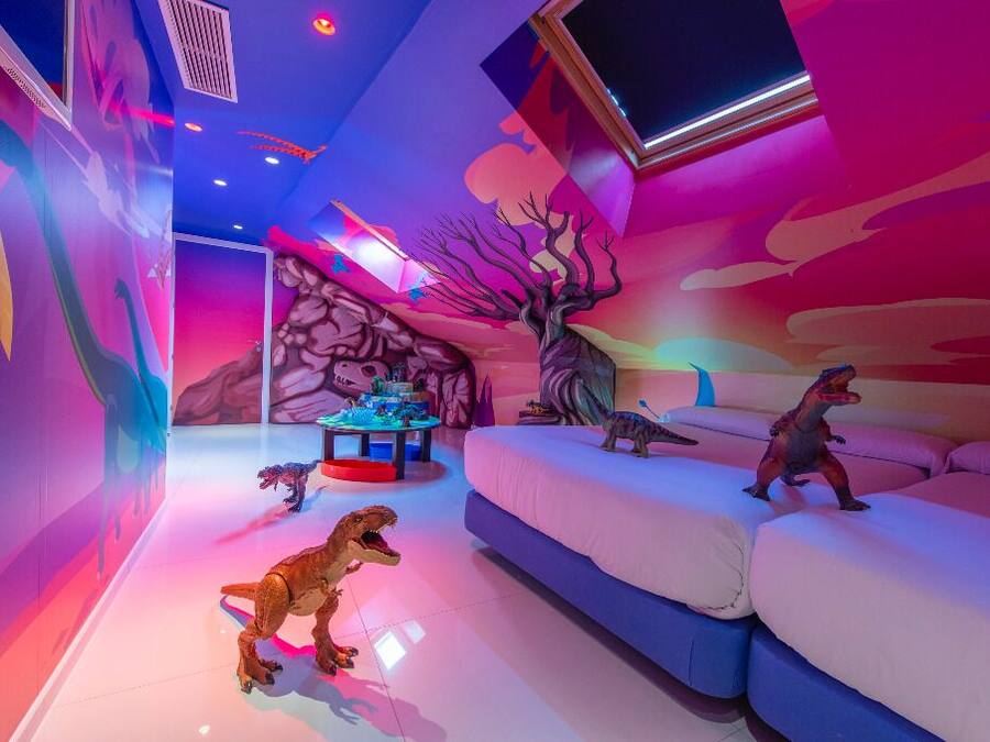 Una habitación decorada con temática de dinosaurios, que incluye un sofá y una mesa con figuras de dinosaurios.