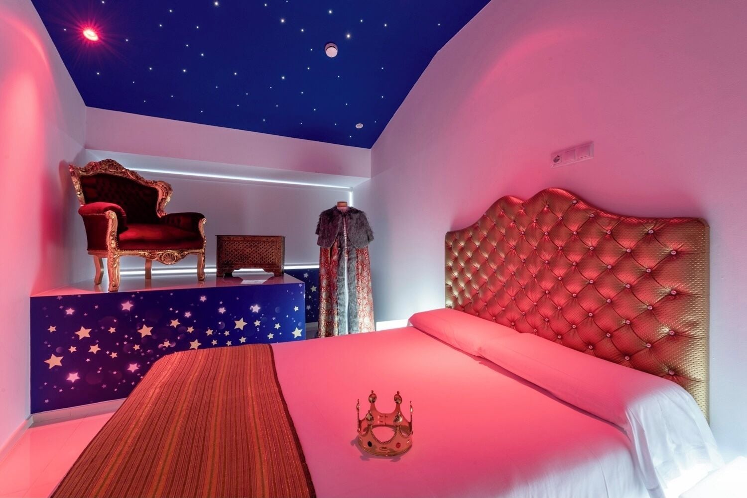 Un dormitorio con techo estrellado, una cama roja, una silla roja y una mesita.