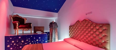 Une chambre avec un plafond étoilé, un lit rouge, une chaise rouge et une petite table.