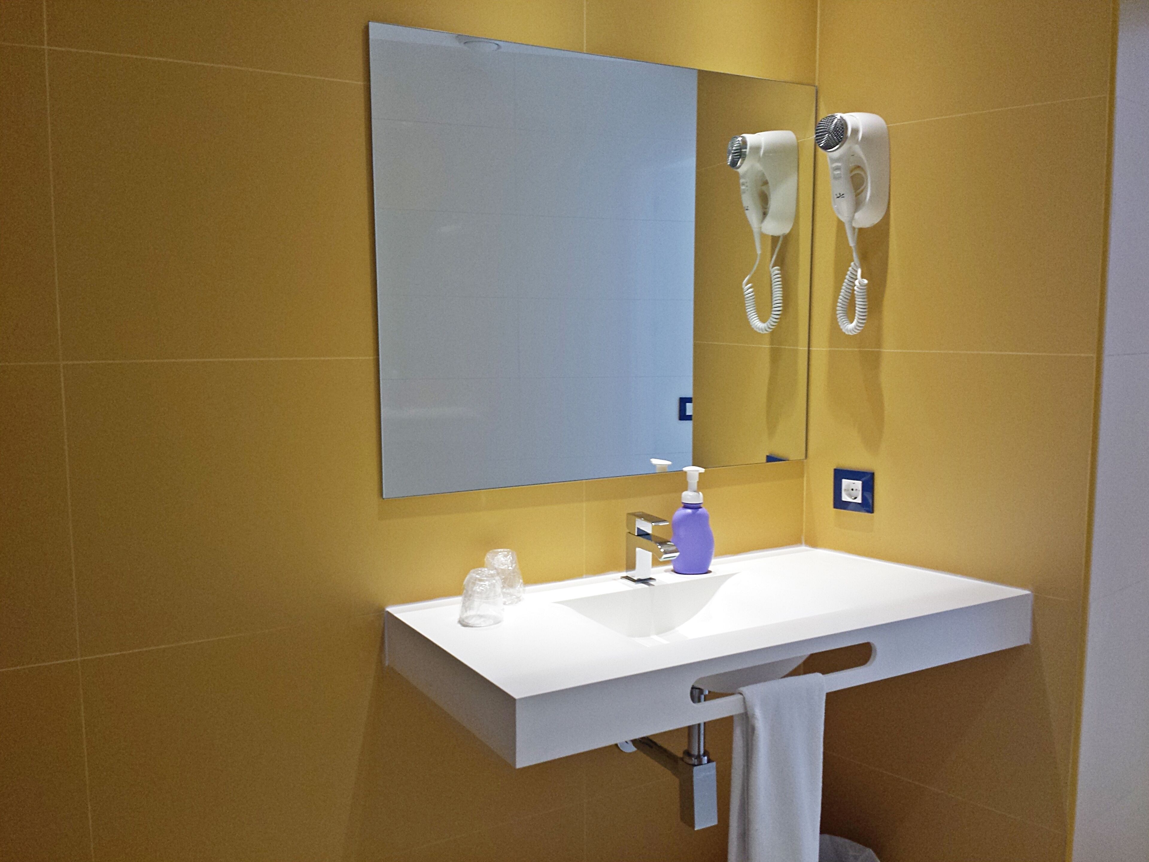 Un baño con lavamanos blanco, un espejo, un secador de pelo y una botella de jabón.